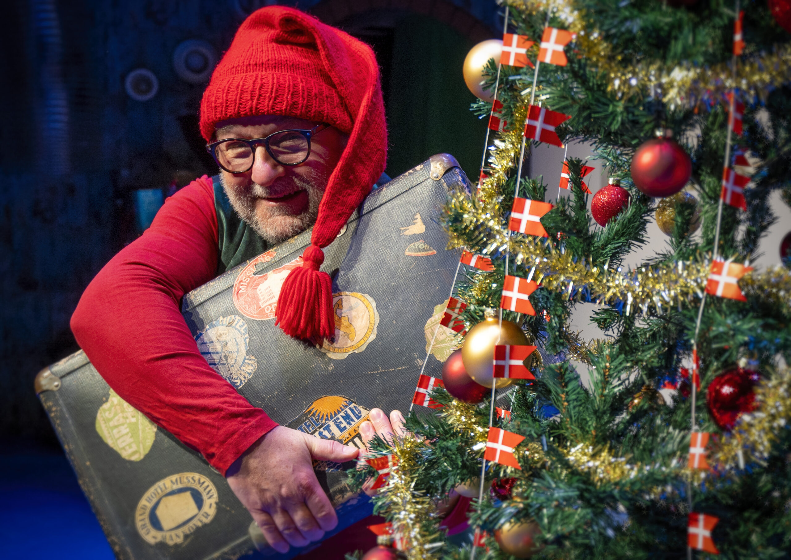 Billedet er en nisse med en kuffert bag et juletræ
